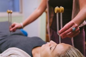 Sound healer holding tuning forks above a woman lying on a treatment table