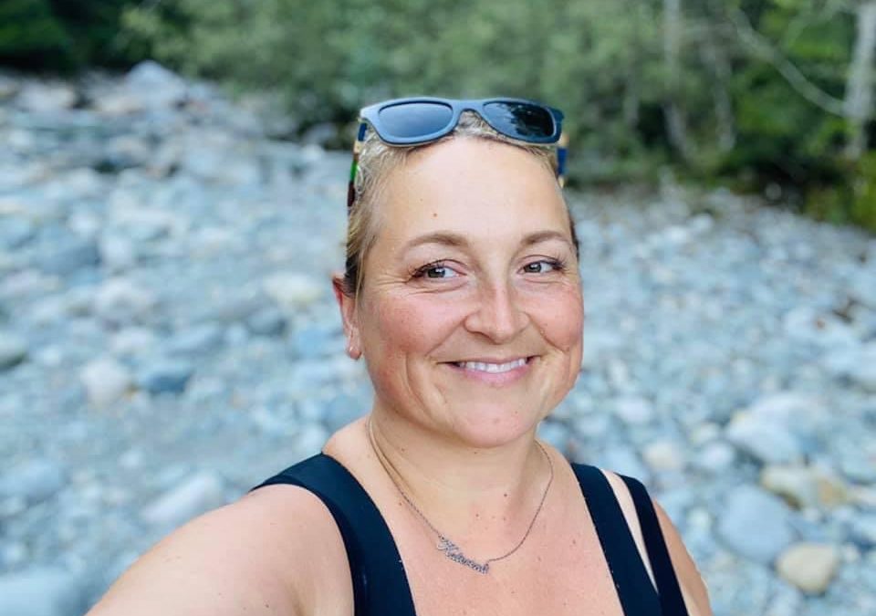 Katerina smiling outdoors on a rocky riverbank with sunglasses on her head