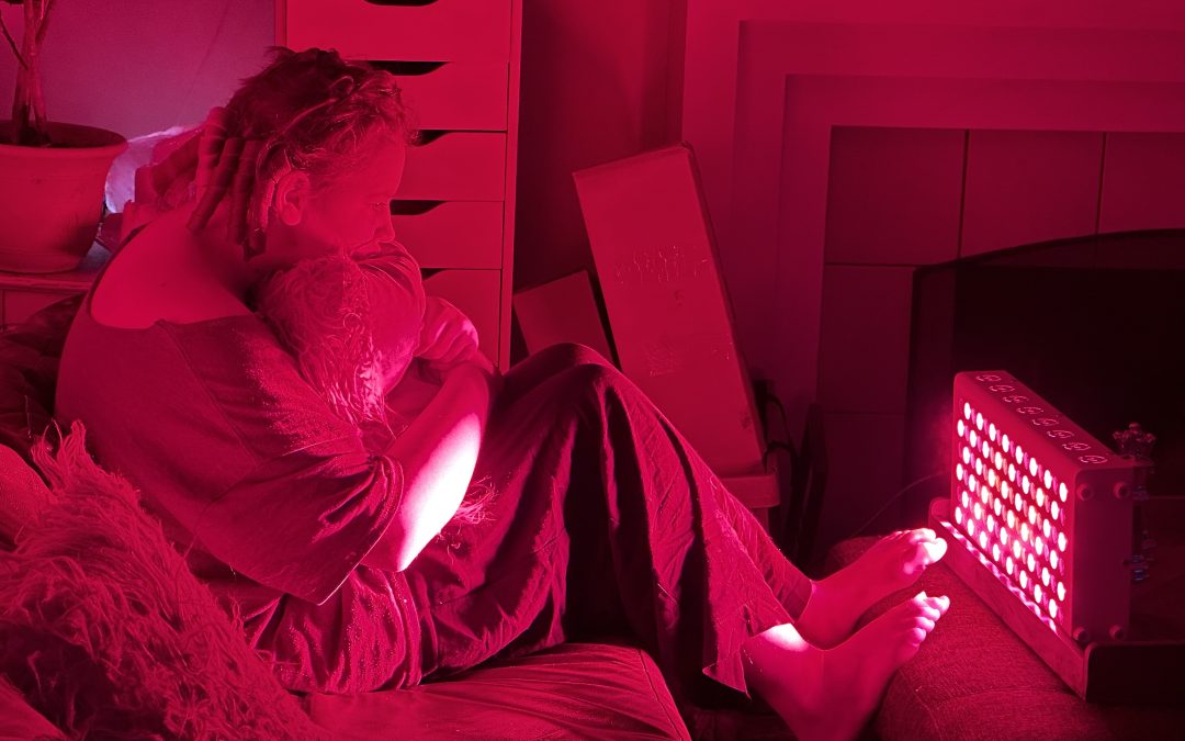 Person relaxing under a red light therapy panel in a dim room