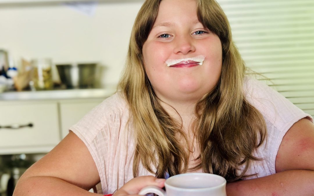 Smiling girl with a milk moustache holding a mug of milk