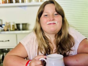 Smiling girl with a milk moustache holding a mug of milk